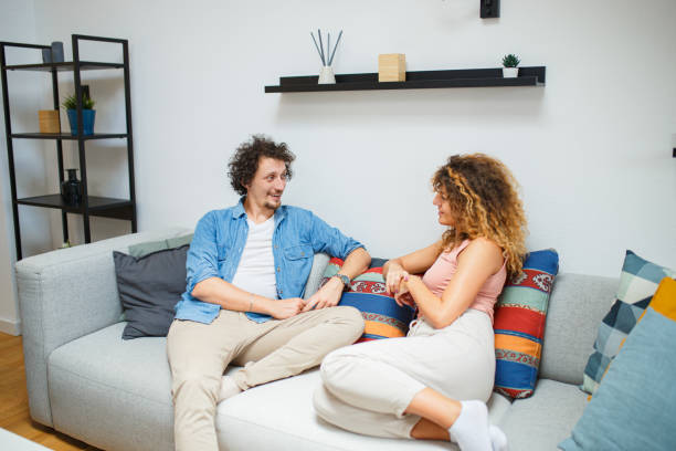 istock Young couple sitting on a sofa in living room, talking 1695336044