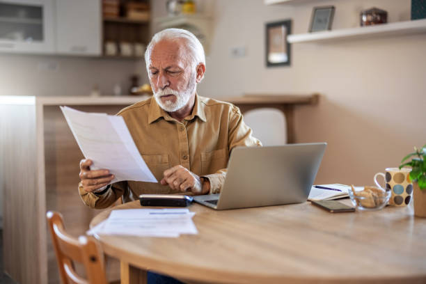 istock Planning, documents and finance with elderly man on laptop in a kitchen, reading retirement and savings plan in his home. thinking, mortgage and investment paperwork with retired male contemplating. 1695336670