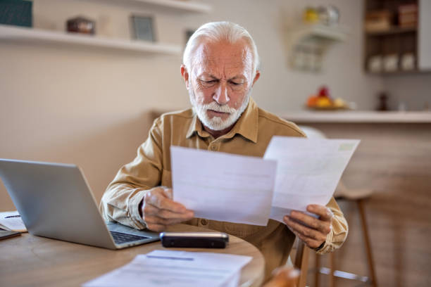 istock Planning, documents and finance with elderly man on laptop in a kitchen, reading retirement and savings plan in his home. thinking, mortgage and investment paperwork with retired male contemplating. 1695336671