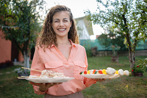 A young Caucasian woman carrying plates with meat, for barbecue