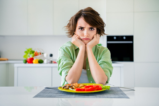Photo of bored sad lady dressed green shirt hands arms cheekbones cheeks having no appetite indoors house kitchen.