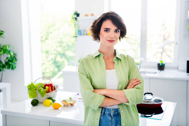 녹색 셔츠를 입은 멋진 자신감 있는 여성의 사진은 실내 집 주방에서 식사를 준비하는 팔짱을 끼고 있습니다 - stereotypical housewife women domestic kitchen brown hair 뉴스 사진 이미지