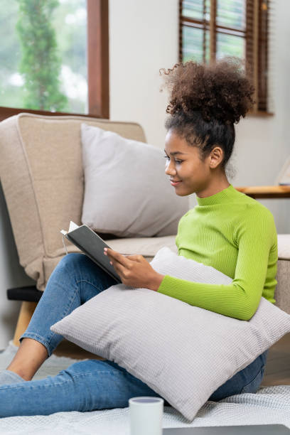 istock Attractive young African woman working on laptop while sitting on sofa at home wearing headset surfing the net using smartphone and tablet while relaxing at home enjoying free time. 1695363104