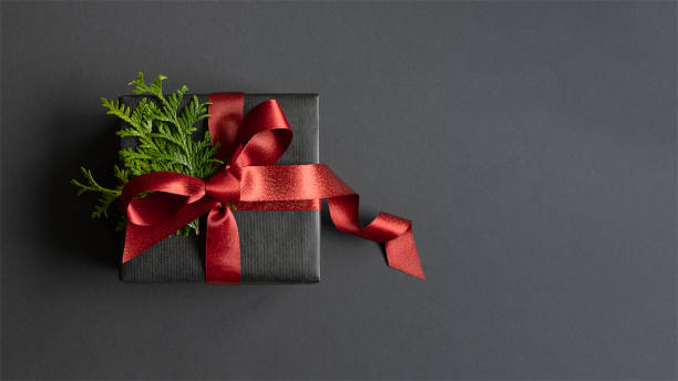 istock Black gift box with thuja and red ribbon on dark background. Flatly, copyspace. 1695373947