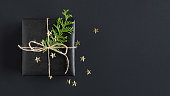Banner with black gift box with thuja and confetti on dark background. Flatly, copyspace.