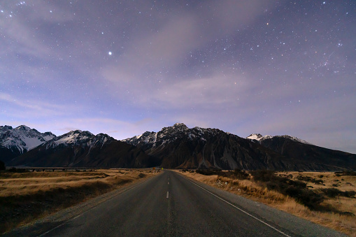 With dawn approaching to the east, stars twinkle above the road to My Cook on New Zealand's South Island.