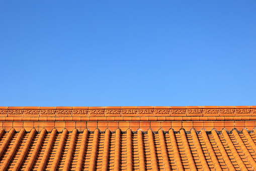 view to a tiled roof with a chimney covered with metal plates on a sunny day with clear blue sky