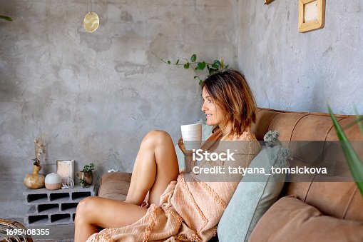 Mother, sitting on the couch at home, drinking coffee, blond toddler child cuddling in her, sleeping