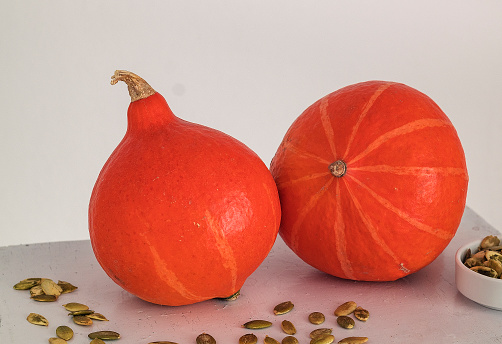 Two fresh orange hokkaido pumpkins and pumpkins seeds on a white background. Copy space.