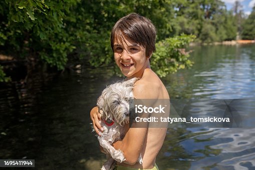 Happy preteen child, boy hugging his dog breed maltese dog at the seashore against a blue sky close up. Best friends rest and have fun on vacation