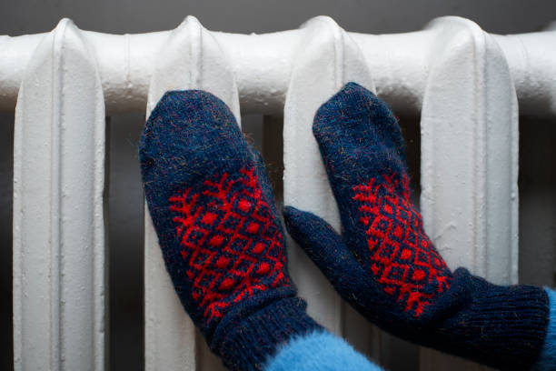 istock Human warming up hands in mittens near Hot Water Radiator. Space for text 1695432063