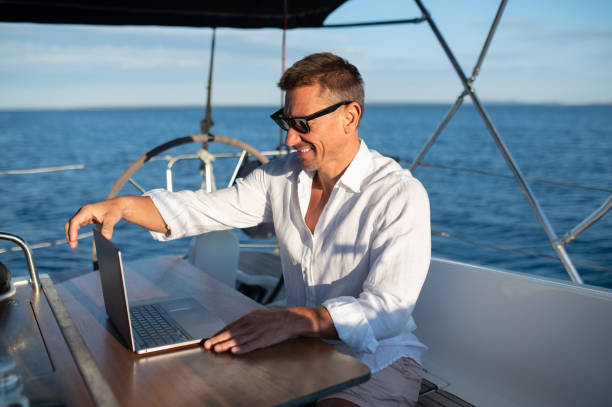 istock Confident man in sunglasses working on a laptop while sailing on a yacht 1695440136