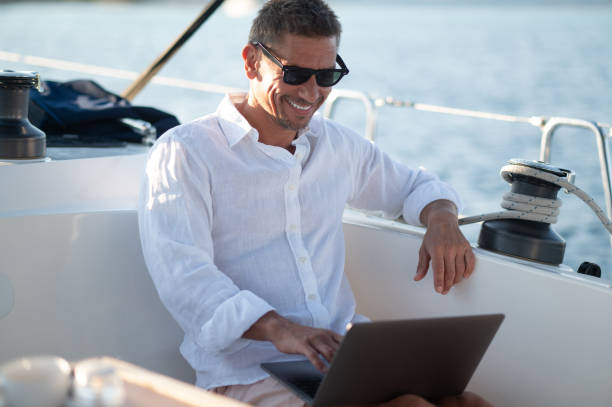 istock Smiling man in sunglasses spending time online while sailing on a yacht 1695440674