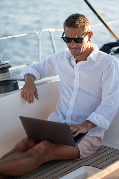 istock Smiling man in sunglasses spending time online while sailing on a yacht 1695440843