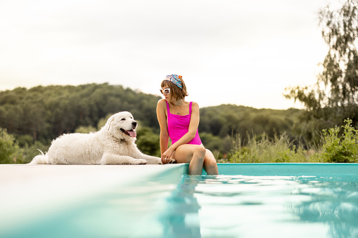 Woman rests with her cute dog near swimming pool, spending summer time together. Concept of friendship with pets and summer vacation