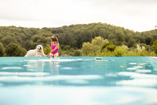 Woman rests with her cute dog near swimming pool, spending summer time together. Concept of friendship with pets and summer vacation