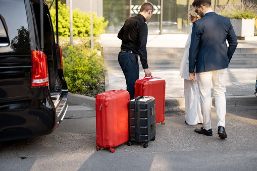Driver or concierge helps a business couple carry their suitcases to the office or hotel from a minivan taxi. Concept of business travel and transportation service