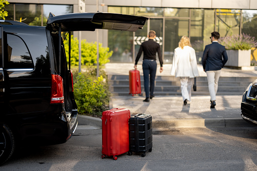 Driver or concierge helps a business couple carry their suitcases to the office or hotel from a minivan taxi. Concept of business travel and transportation service