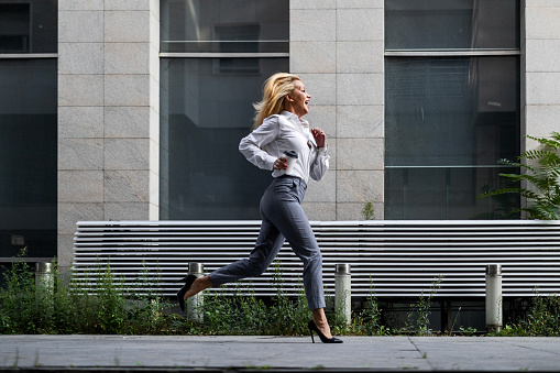 Businesswoman outside office building with laptop bag holding a coffee running