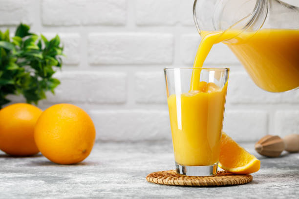 istock orange juice pouring into glass from jug on table in kitchen 1695497533