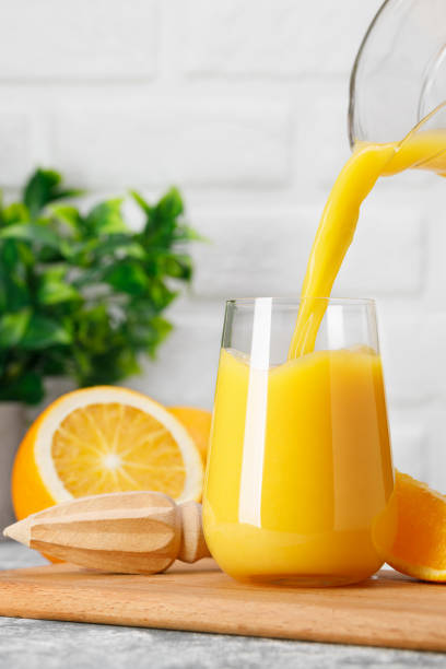 istock orange juice pouring into glass from jug on table 1695497534