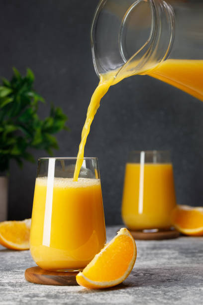 orange juice pouring into glass from jug on table