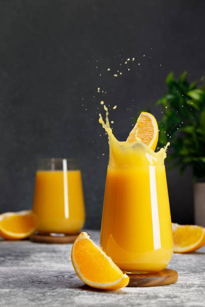 istock orange juice in glass with splash and falling slice of fruit on table 1695497595