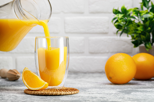 orange juice pouring into double wall glass from jug on table in white kitchen