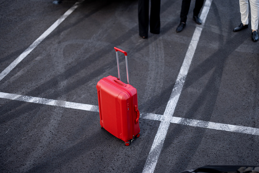 Red suitcase on asphalt of parking lot outdoors, concept of business travel