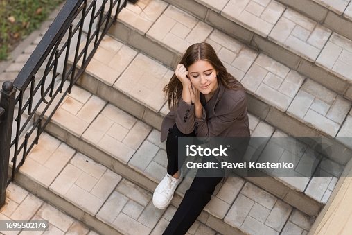 Portrait of a Caucasian attractive and happy young woman in casual clothes sitting on the steps in the city while walking. The concept of style, fashion, youth and lifestyle. Aerial view