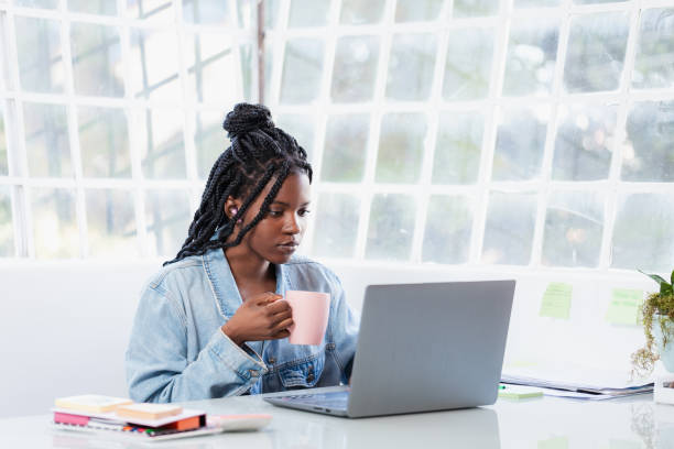 istock Young woman holding a mug and working on her computer at home office 1695509201