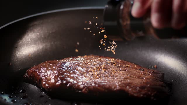 Seasoning is poured onto a cut of meat in a frying pan