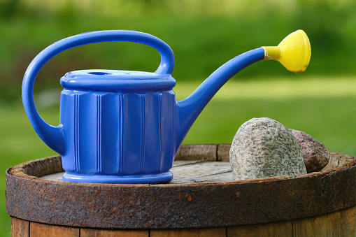 Blue garden watering can on vintage barrel. Shallow depth of field