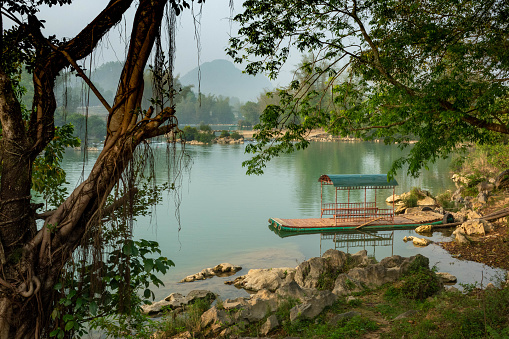 Boat (small ferry) in a river near Cao Bang, North Vietnam. Tree in the foreground; mountains in the background
