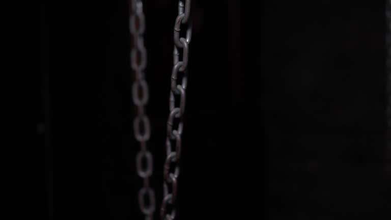 Hanging metal chains in a dark room, chains swinging from side to side.