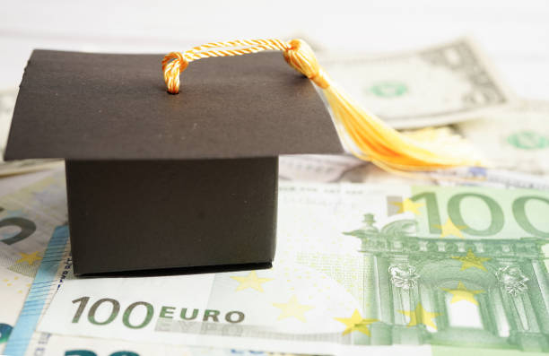 istock Graduation gap hat on Euro and US dollar banknotes money, Education study fee learning teach concept. 1695589921