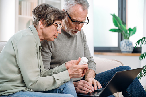 elderly couple using laptop, searching medication on pharmacy website to make online order. mature man and woman have medical consultation with doctor by chat on notebook.