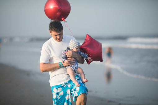 Cheerful young Father with his infant son having fun together by seaside, dad throwing up kid in the air