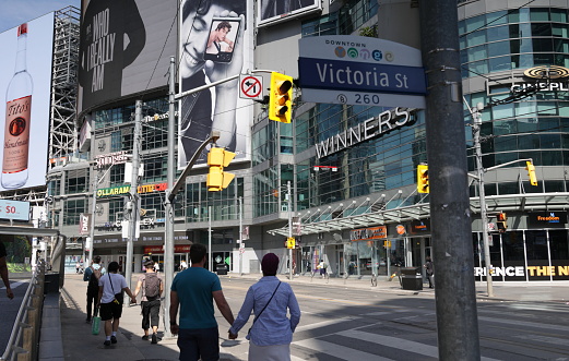 Toronto, Canada - August 22, 2023: Pedestrians walk west along Dundas Street East by Yonge-Dundas Square. Across the street stands The Tenor, an entertainment and shopping complex at 10 Dundas Street East.