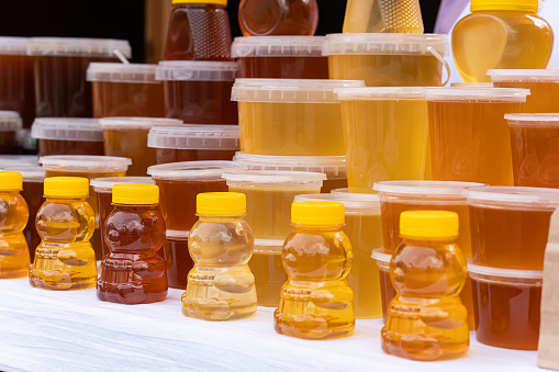 There are many jars of organic, natural honey on counter for sale. Different honey, different colors in plastic cans are ready for sale at the honey fair. Nuts filled with honey.
