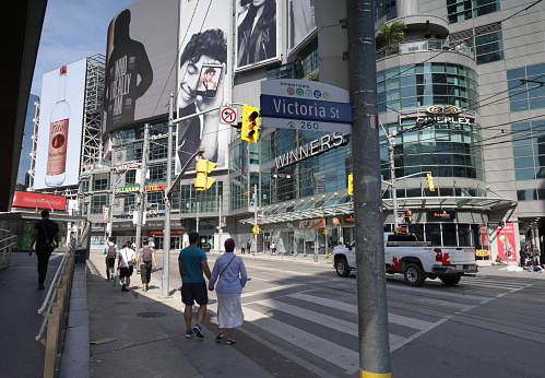 Toronto, Canada - August 22, 2023: Pedestrians wait at the crosswalk on Dundas Street East at the 200-block of Victoria Street. The Tenor entertainment complex stands north at 10 Dundas Street East.