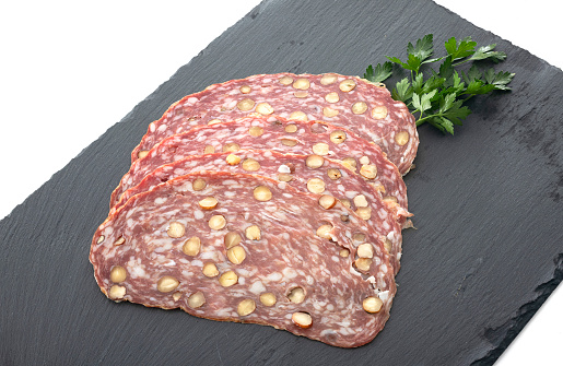 Sliced dry sausage with hazelnut in front of white background