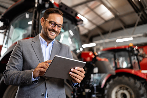 Tractor dealer standing in workshop preparing agricultural machines for sale.