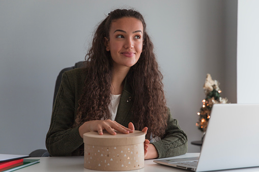 Happy young businesswoman acting surprised upon opening a Christmas gift