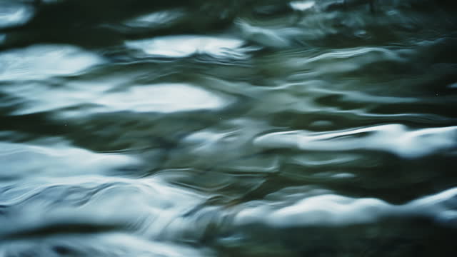 SLO MO Close-Up of Sunlight Reflecting Flowing River Water Surface Creating Wave Pattern