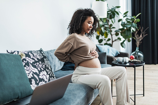 Pregnant black woman sitting on sofa and suffering pain in back