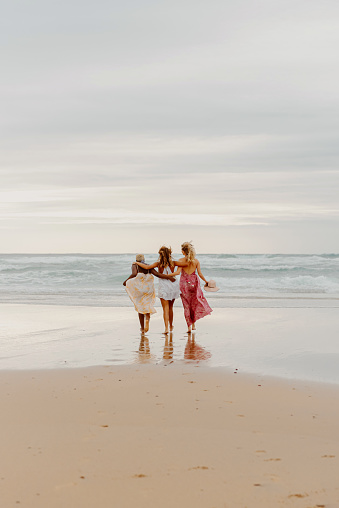vertical photo on the beach of multiracial group of three young women walking towards the water. friendship and summer concept