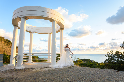 Portrait of a bride in a wedding dress in a beautiful gazebo with columns on the seashore