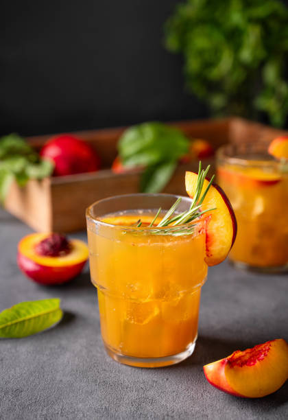 thé aux pêches avec glace et romarin sur un verre. boisson saine végétalienne faite maison sur un fond sombre avec des fruits frais. - georgia peach photos et images de collection