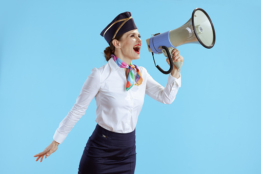 happy stylish stewardess woman against blue background in uniform with megaphone.